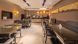 A modern dining area with long tables and chairs, a kitchen in the background, and a large abstract painting on the wall. - Ripple Hotel (Sihong Renmin Road) (Sihong)