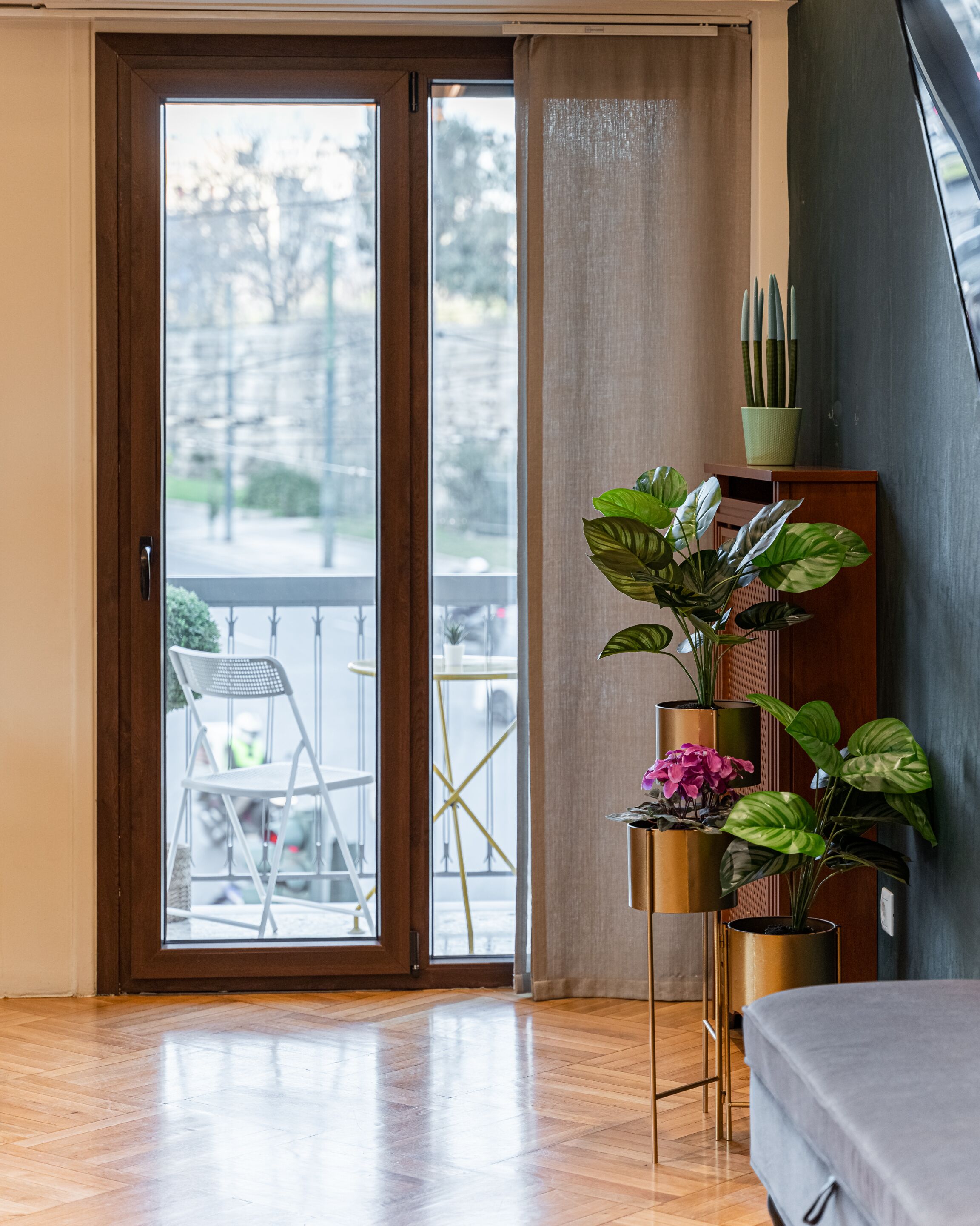 A room with a sliding glass door leading to an outdoor area with a chair and table. There are several potted plants on a stand near the door.