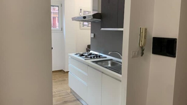 Une cuisine compacte avec des meubles blancs, une cuisinière à gaz et un évier moderne.