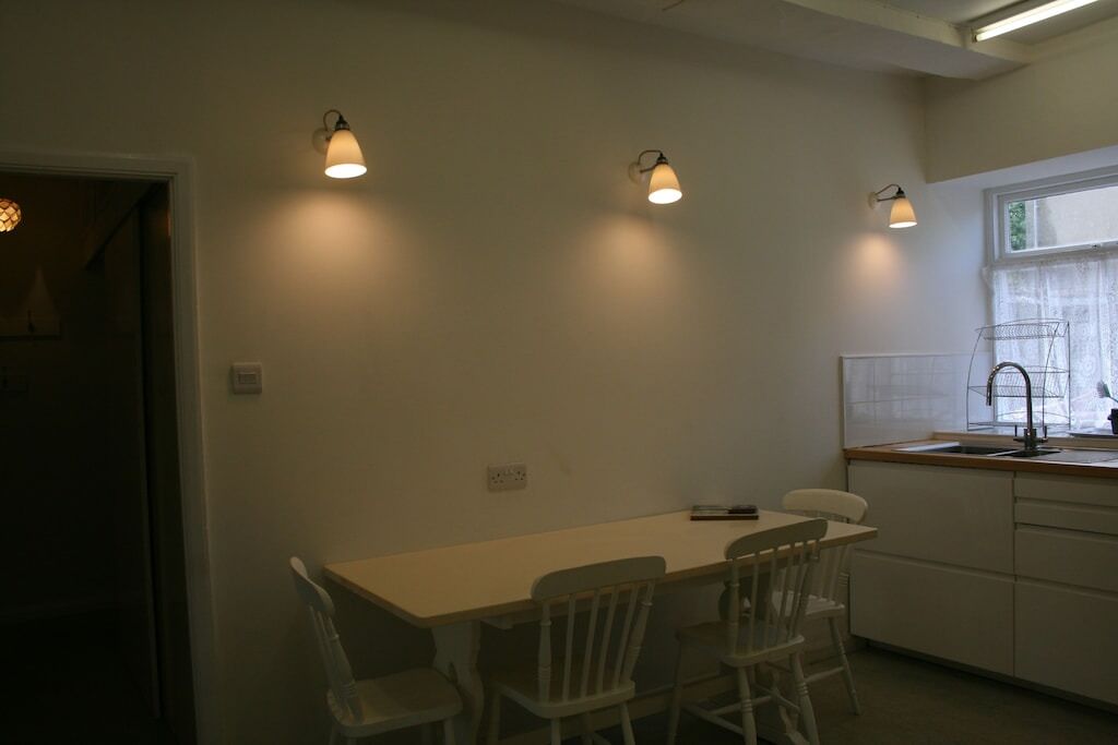 Une petite cuisine avec une table et des chaises, une fenêtre donnant sur un beau paysage et des lampes fixées au mur.