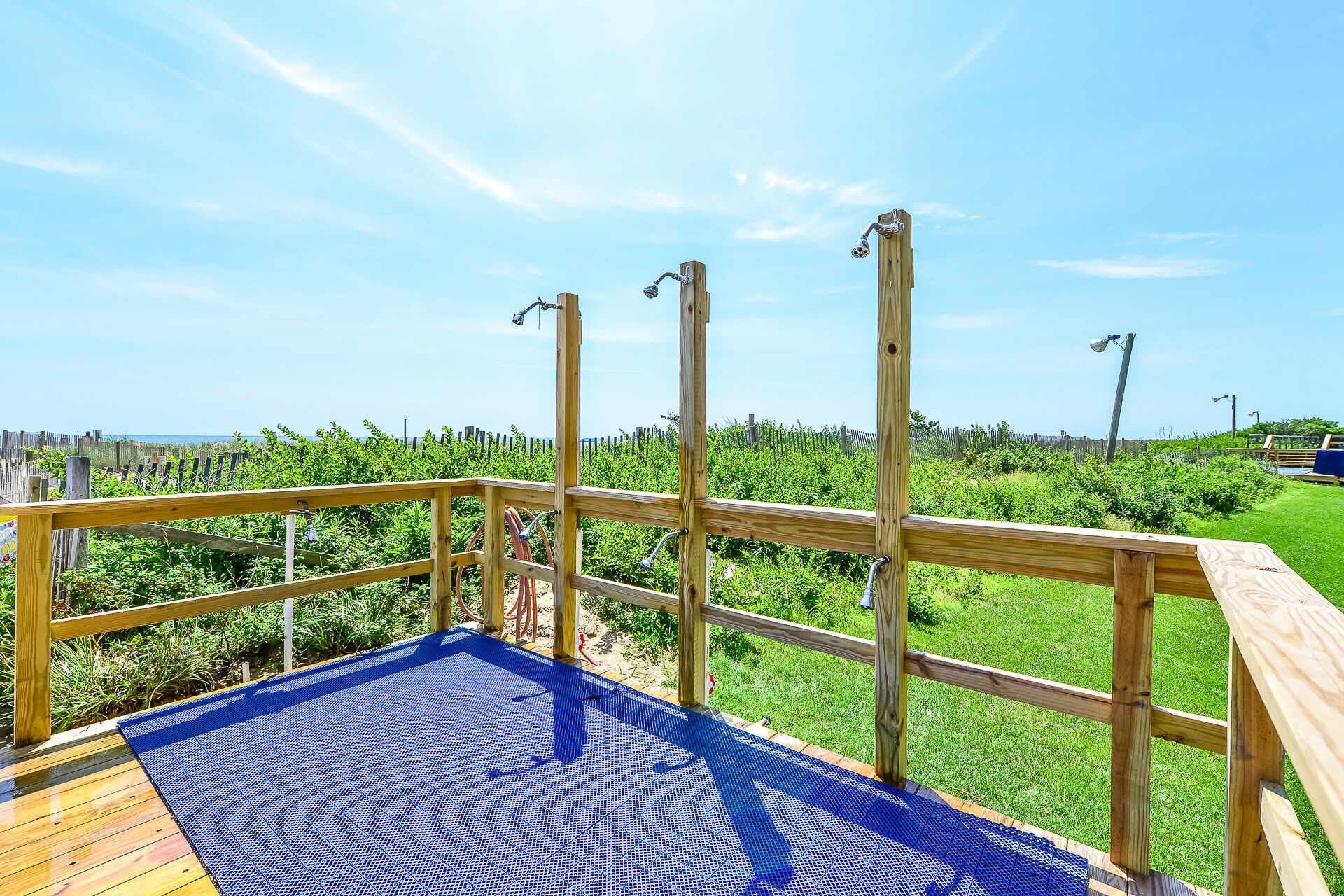A wooden deck with a blue safety mat, metal railings, and a view of a grassy area with a fence and a body of water in the background.