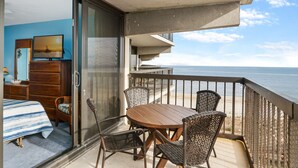A balcony with a wooden table and wicker chairs, overlooking a beach. - Beautifully updated 2 bedroom condo by Seaside Vacations & Sales (Ocean City)