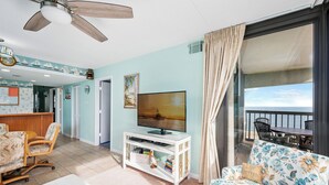 Ein Wohnzimmer mit Fernseher, einer Couch, einem Essbereich und einem Balkon mit Meerblick.