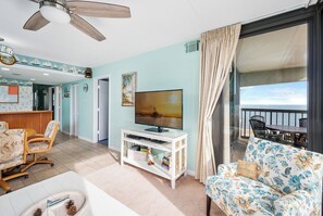 A living room with a TV, a sofa, a dining area, and a balcony with a view of the sea. - Beautifully updated 2 bedroom condo by Seaside Vacations & Sales (Ocean City)