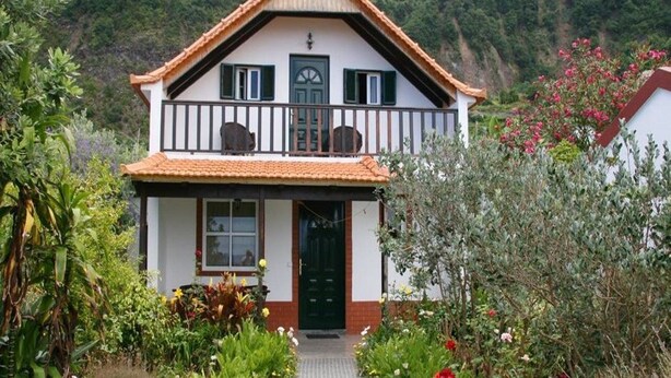 A two-story house with a balcony, surrounded by a garden with various plants and flowers. - Quinta da Quebrada (Santana)