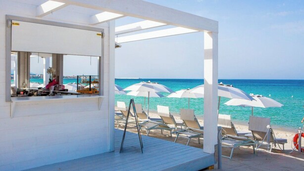 Een strandhut aan het strand, met een bar, witte parasols en comfortabele ligbedden.