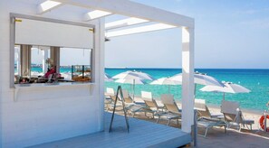 Un cabanon de plage avec un coin bar, des parasols blancs et des chaises longues.