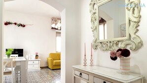Een kamer met een witte console, een spiegel en een vaas met bloemen. Er staan een gele stoel en een witte stoel in de kamer.