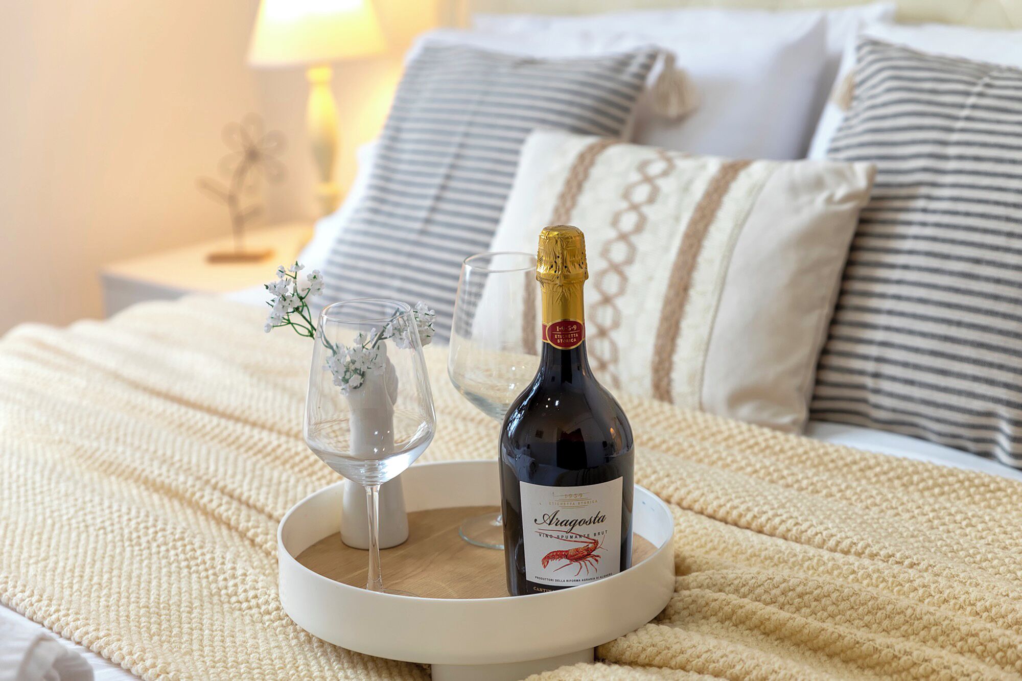 Een bed met een witte deken, een fles wijn en een glas op een dienblad.