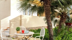 Een terras met een ronde tafel en vier stoelen, omringd door weelderige begroeiing en palmbomen.