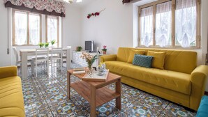 Een woonkamer met een gele bank, een houten salontafel en een eethoek met een witte tafel en stoelen.