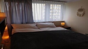 Ein ordentlich bezogenes Bett mit weißen Leinen, eine Nachttischlampe und ein Traumfänger an der Wand.