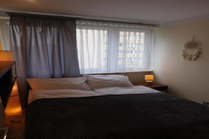 A neatly made bed with white linens, a bedside lamp, and a dreamcatcher on the wall.