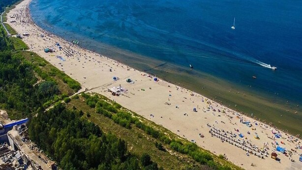 Luftaufnahme eines Strandes mit einer gewundenen Küstenlinie, klarem, blauem Wasser und einigen Booten.