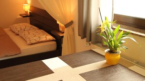 Et hotelværelse med en seng, et natbord med lampe, en potteplante og et vindue med gardiner.