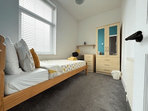 A bedroom with a single bed, a dresser, a wardrobe, and a window with blinds.