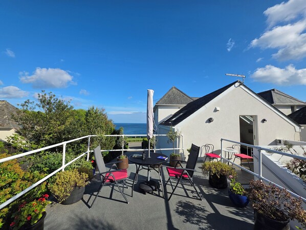 A rooftop terrace with a table and chairs, potted plants, and a view of the sea.