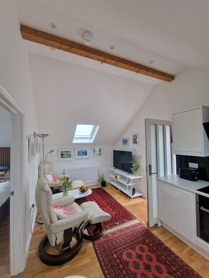 A modern living room with a high ceiling, a skylight, a white sofa, a TV, and a kitchen area.