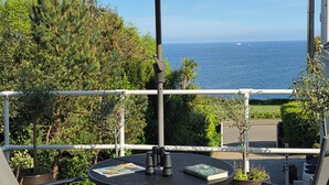 Varanda com mesa, cadeiras e guarda-sol, com vista para o mar.