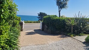Um caminho pavimentado leva a um portão, ladeado por vegetação exuberante e com vista para o mar.
