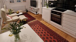 Cozinha moderna com armários brancos, fogão preto e bancada branca. Há uma área de jantar com mesa branca e tapete vermelho estampado.