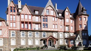 Un grand bâtiment historique à plusieurs étages, caractérisé par un mélange de maçonnerie en pierre et de charpente en bois, et doté d’une entrée imposante surmontée d’un petit porche.