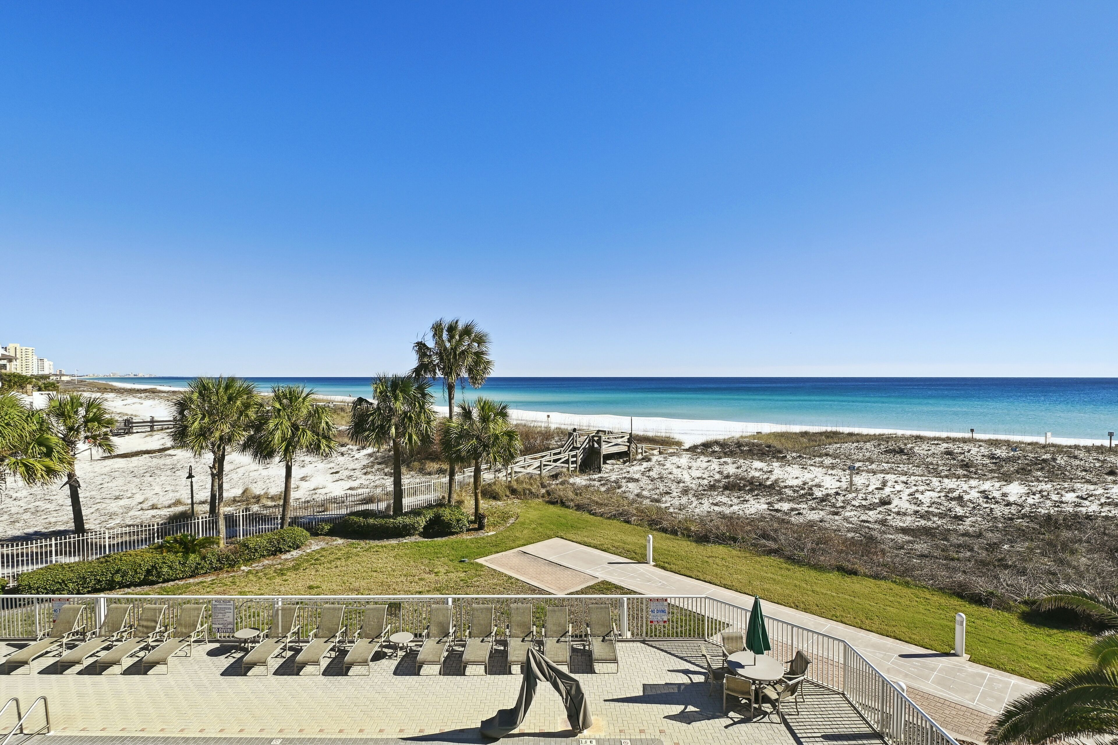 A beach view with a patio area, palm trees, and a sandy beach.