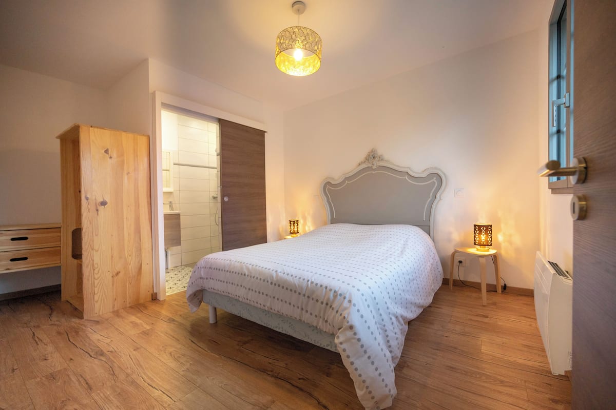 A bedroom with a wooden floor, a bed with a white duvet, two bedside lamps, and a wooden wardrobe.