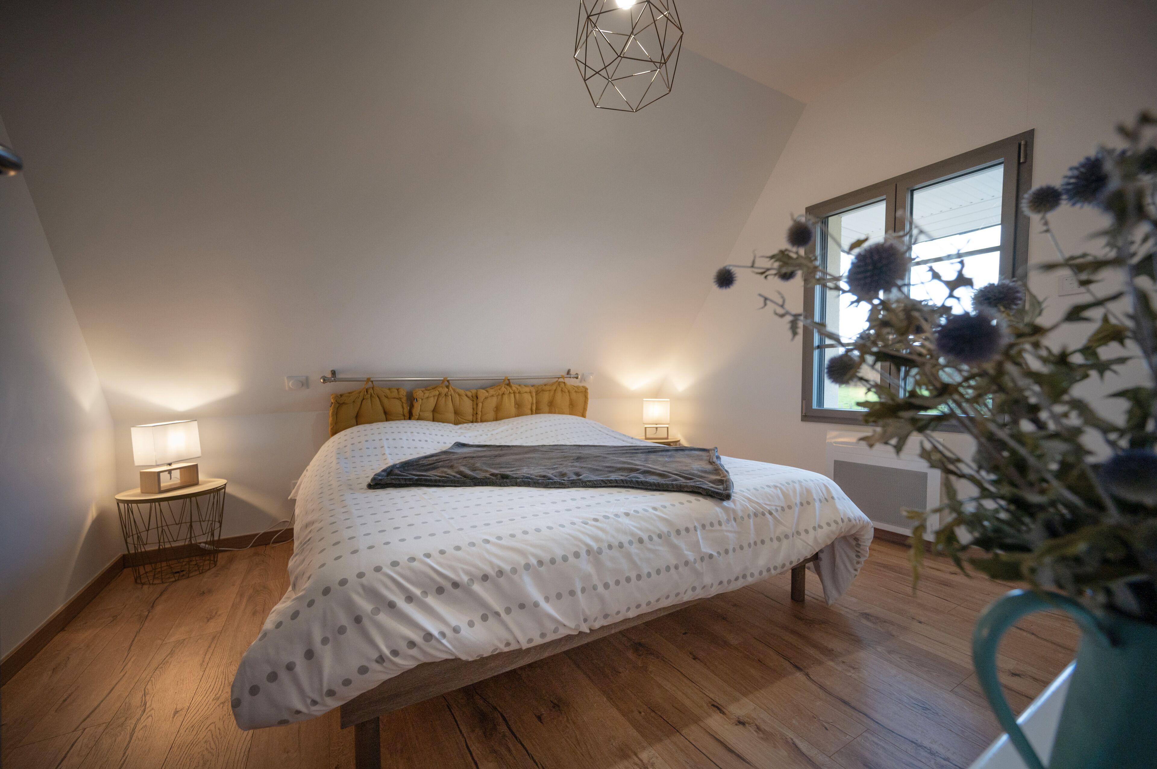 A bedroom with a bed, two bedside tables with lamps, a window with a view, and a ceiling light fixture.