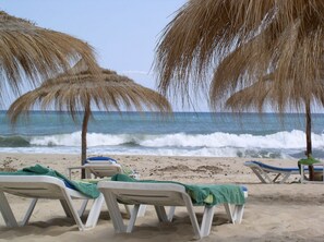 En strand med vita solstolar och parasoller med halmtak.