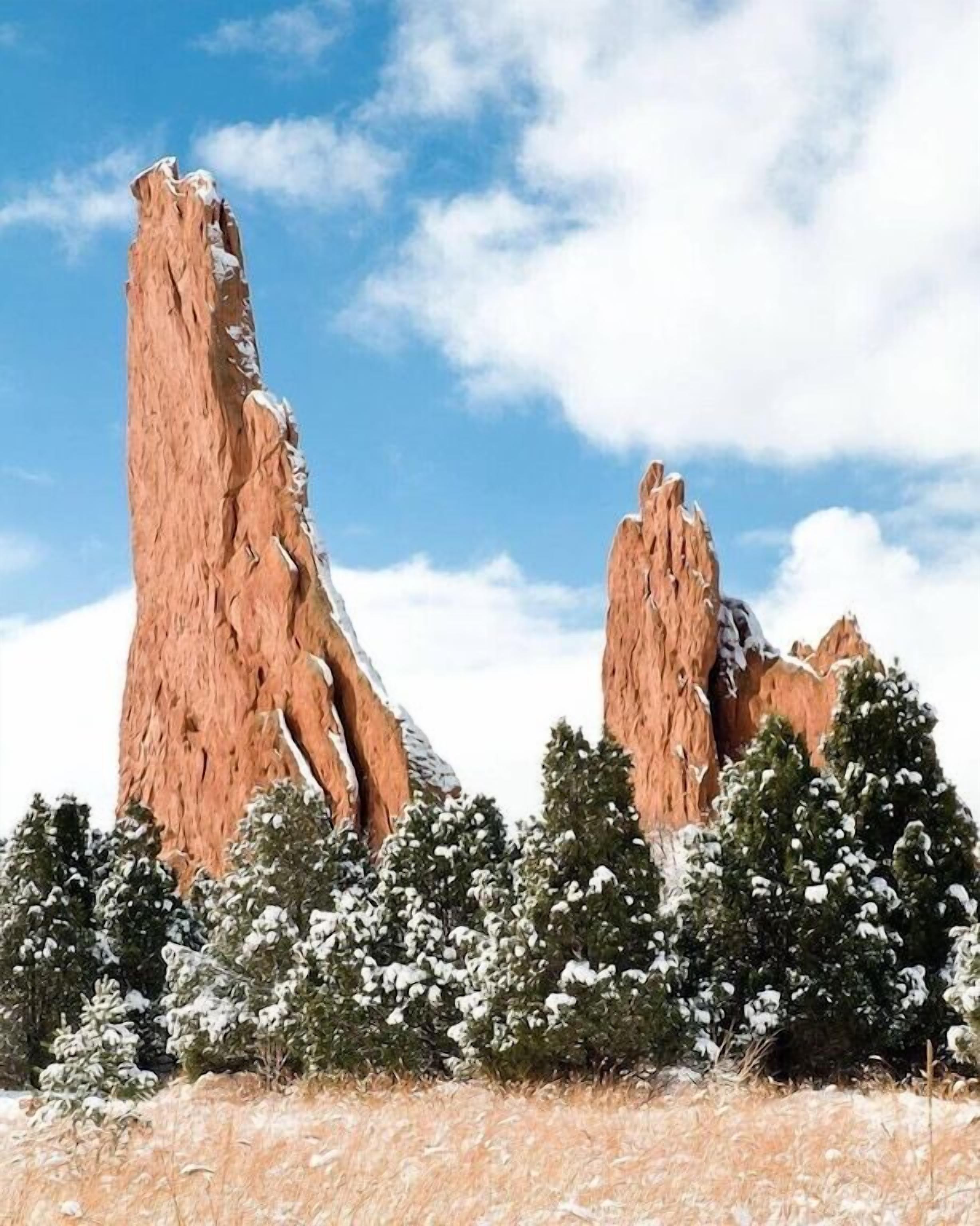A tall, rugged rock formation with snow-covered trees in the foreground.