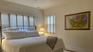 A bedroom with a large bed, white bedding, a bedside lamp, and a painting on the wall. - Cozy, Romantic, Secluded, Cottage in the Heart of Cheyenne Cañon (Colorado Springs)