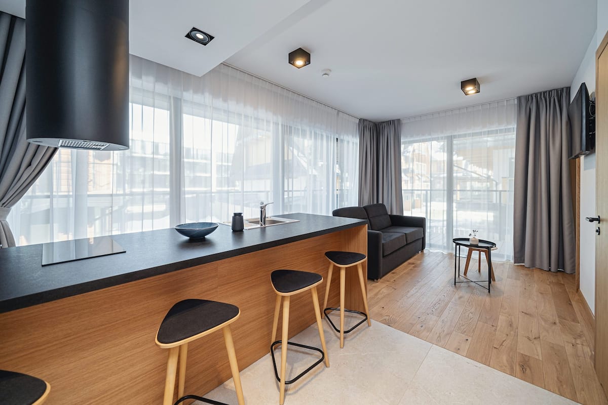 A modern kitchen with a central island, bar stools, a sofa, and a TV mounted on the wall.