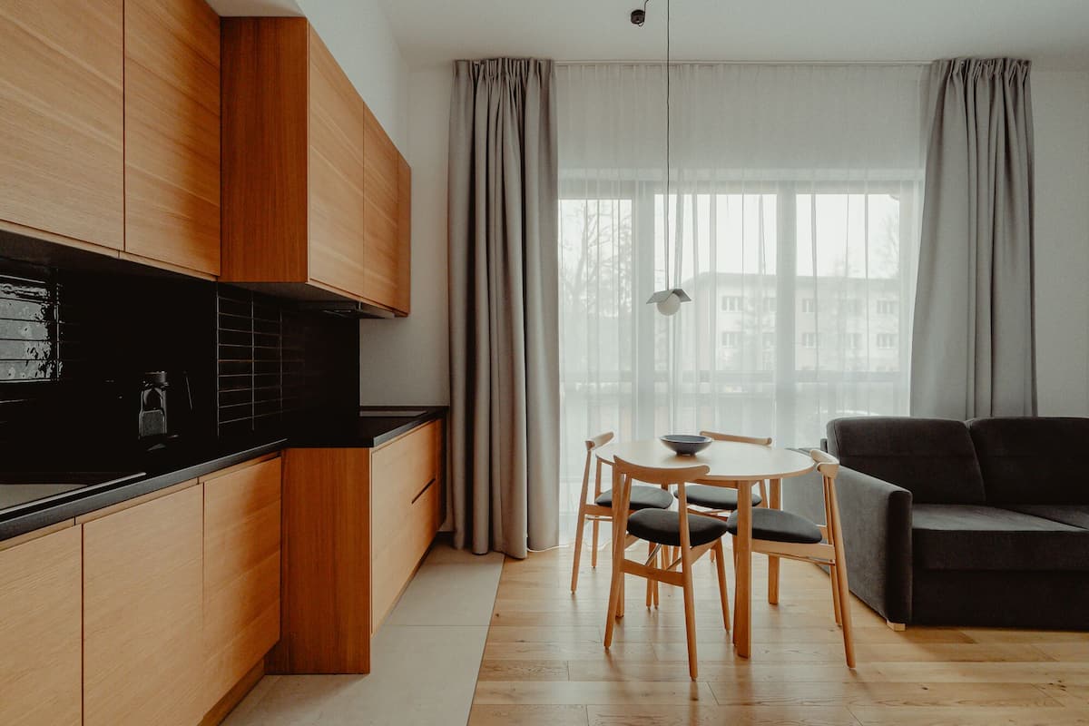 A modern kitchen with wooden cabinets, a black countertop, and a dining area with a round table and chairs.