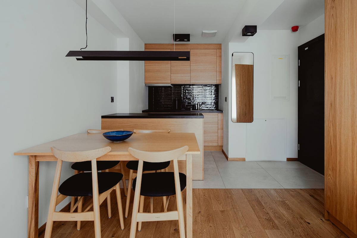A compact kitchen with wooden cabinets, a black countertop, and a dining area with a wooden table and black chairs.