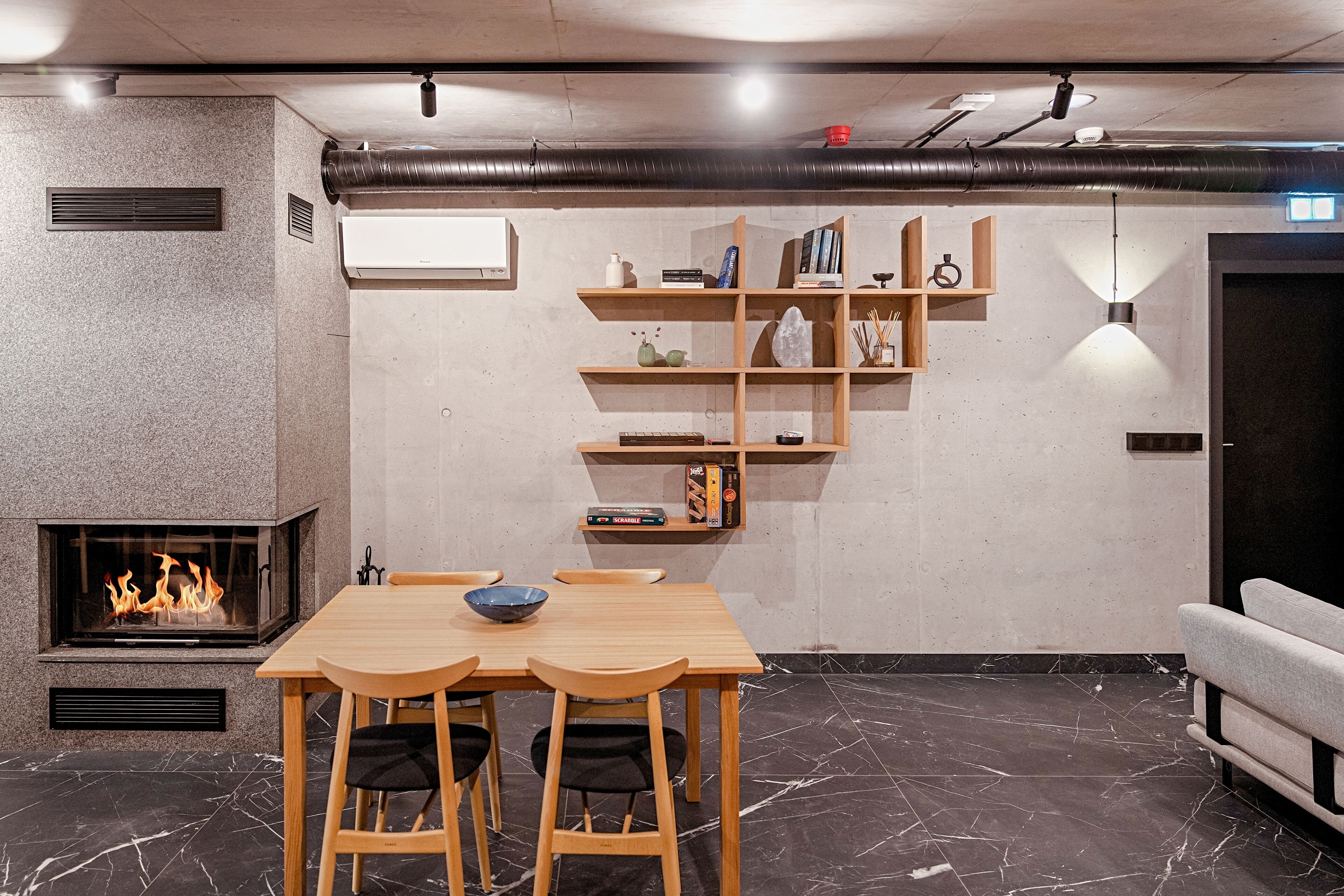 A modern dining area with a fireplace, wooden table, chairs, and a built-in bookshelf.