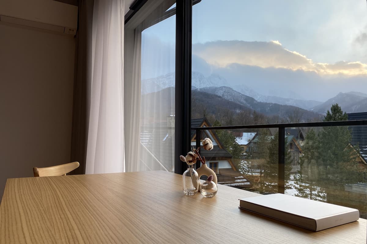 A room with a large window offering a view of snow-capped mountains and a cabin.