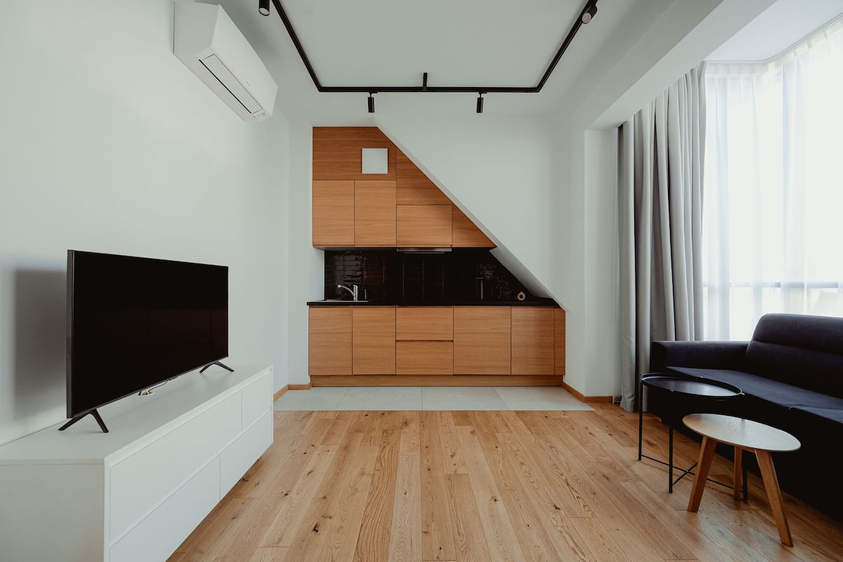 A modern living space with a TV, a sofa, a small table, and a kitchen area with wooden cabinets and a black countertop.