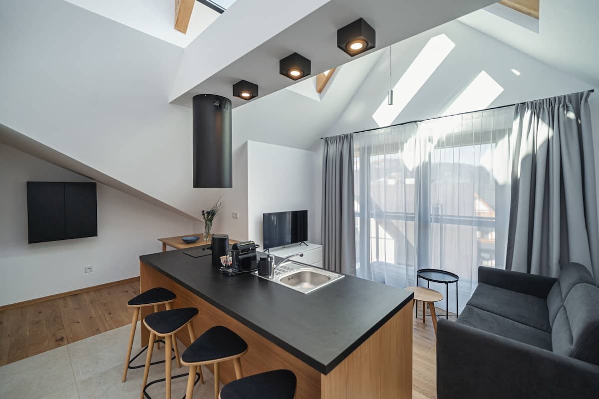 A modern kitchen with a central island, bar stools, a built-in oven, and a large window with curtains.