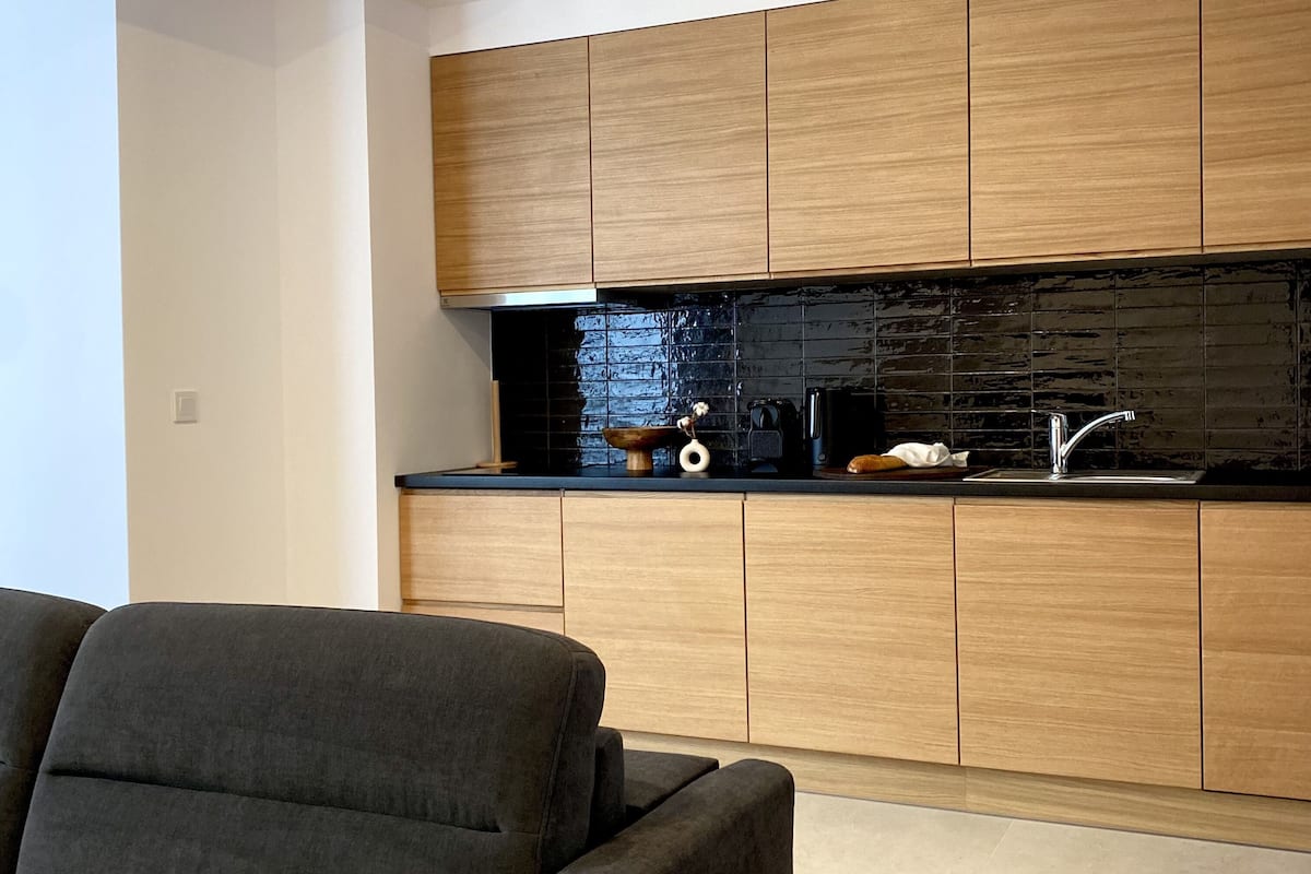 A modern kitchen with wooden cabinets, a black backsplash, and a stainless steel sink.