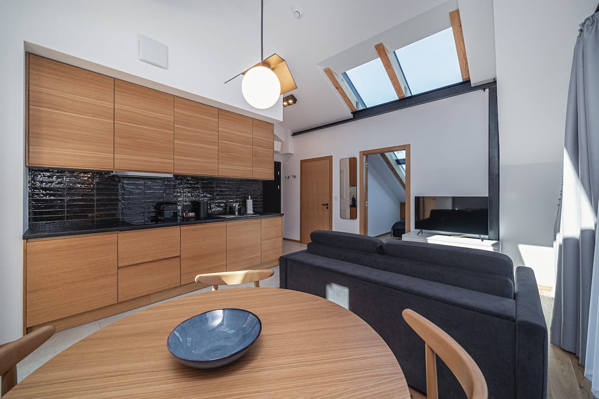A modern kitchen with wooden cabinets, a black backsplash, and a dining area with a round table and chairs.