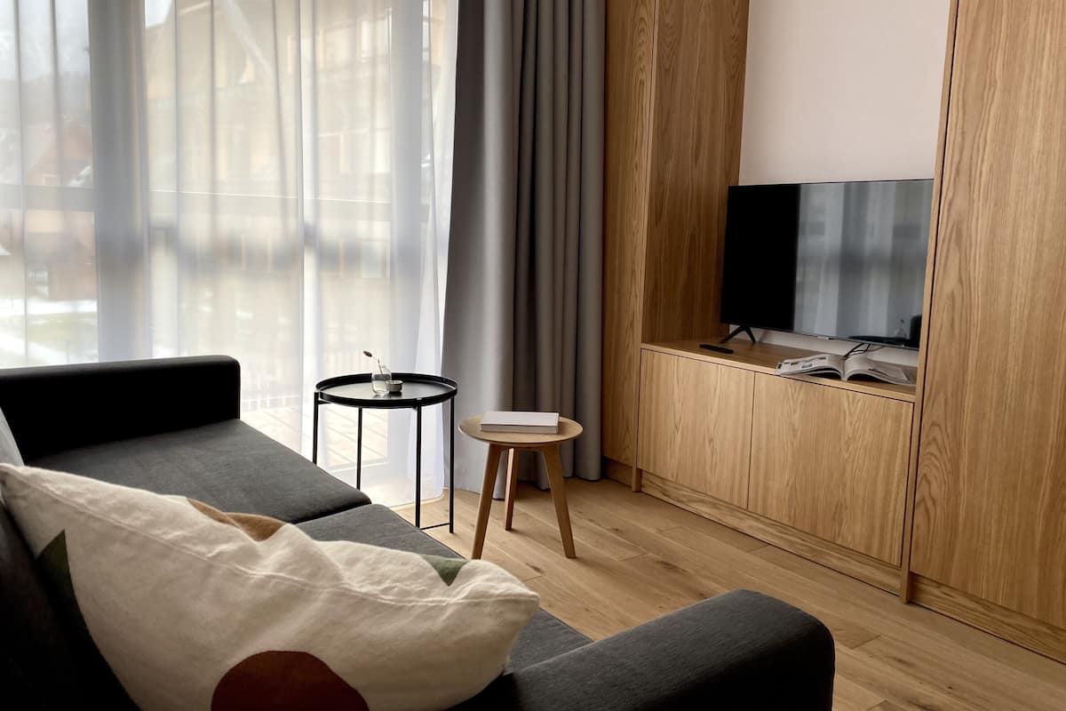 A modern living room with a sofa, a small round table with a glass, and a TV on a wooden cabinet.
