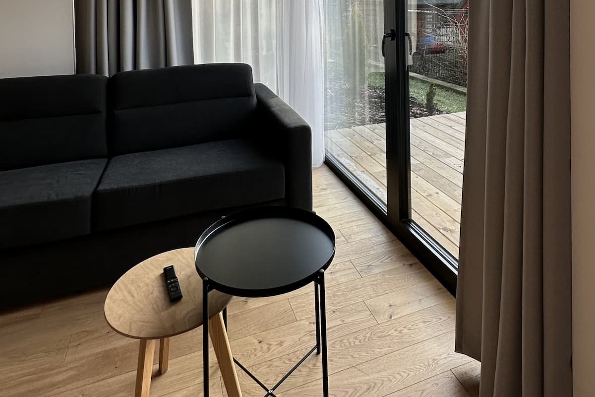 A modern living room with a dark sofa, a small round table, and a sliding glass door leading to a wooden deck.