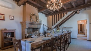 A dining area with a long wooden table set for a meal, flanked by chairs with woven seats. A fireplace with a stone mantle is visible in the background, and a chandelier hangs from the ceiling. - Casale Andrea - 7 bedrooms, pool, airco, wifi, pet friendly, Umbria (Spoleto)