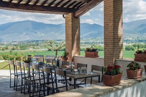 An outdoor dining area with tables and chairs, potted plants, and a view of mountains and a green landscape. - Casale Andrea - 7 bedrooms, pool, airco, wifi, pet friendly, Umbria (Spoleto)