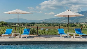 A poolside area with blue lounge chairs and white umbrellas, overlooking a scenic landscape with mountains and fields. - Casale Andrea - 7 bedrooms, pool, airco, wifi, pet friendly, Umbria (Spoleto)