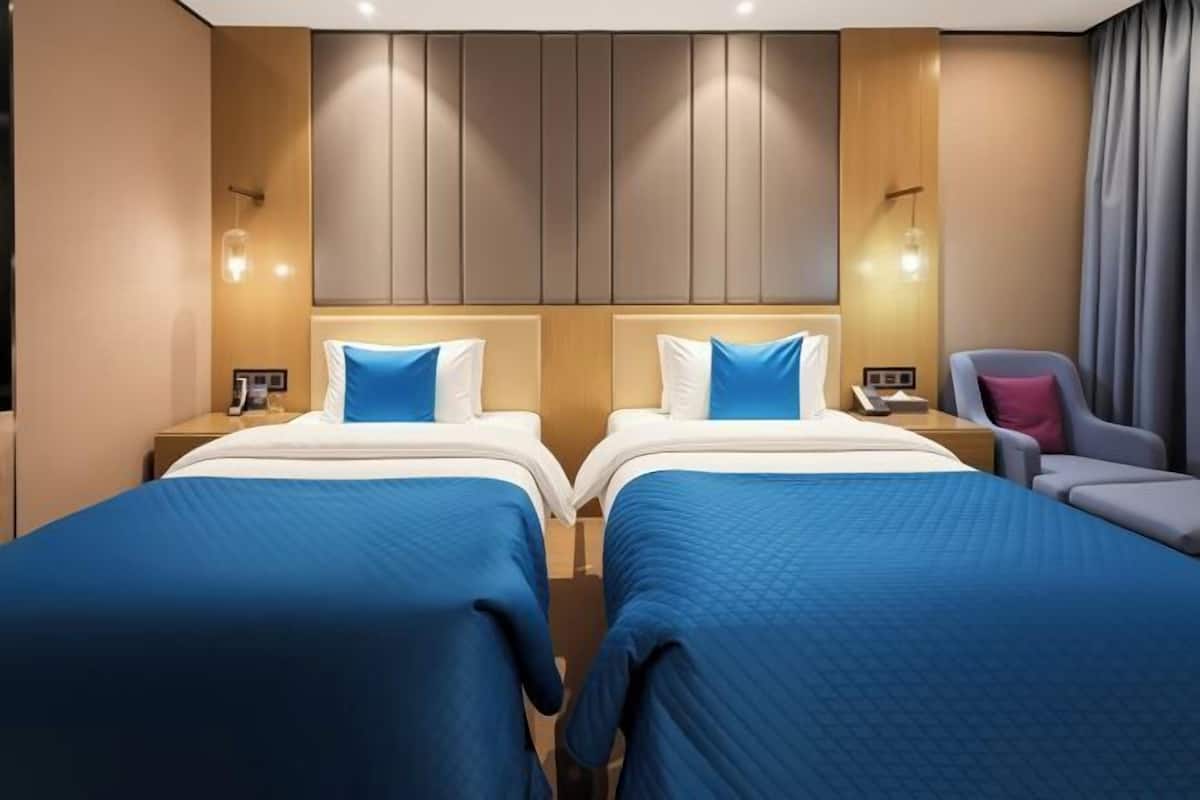A hotel room with two beds, a chair, and a nightstand with a lamp.