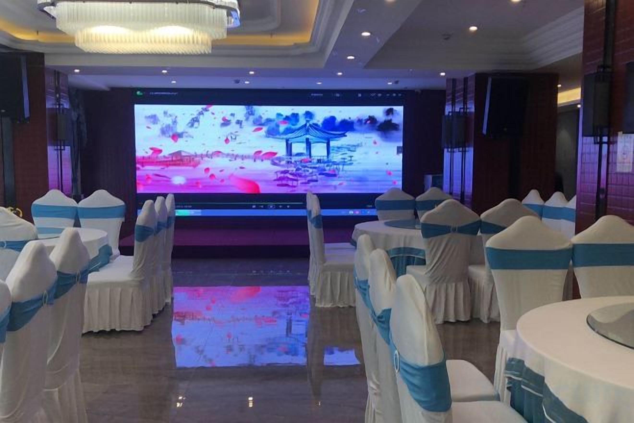 A banquet hall with rows of tables and chairs, a large screen at the front, and a chandelier.