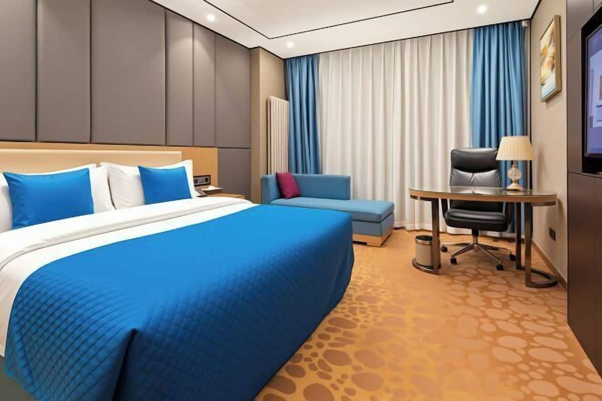 A hotel room with a large bed, a desk, a chair, and a television.