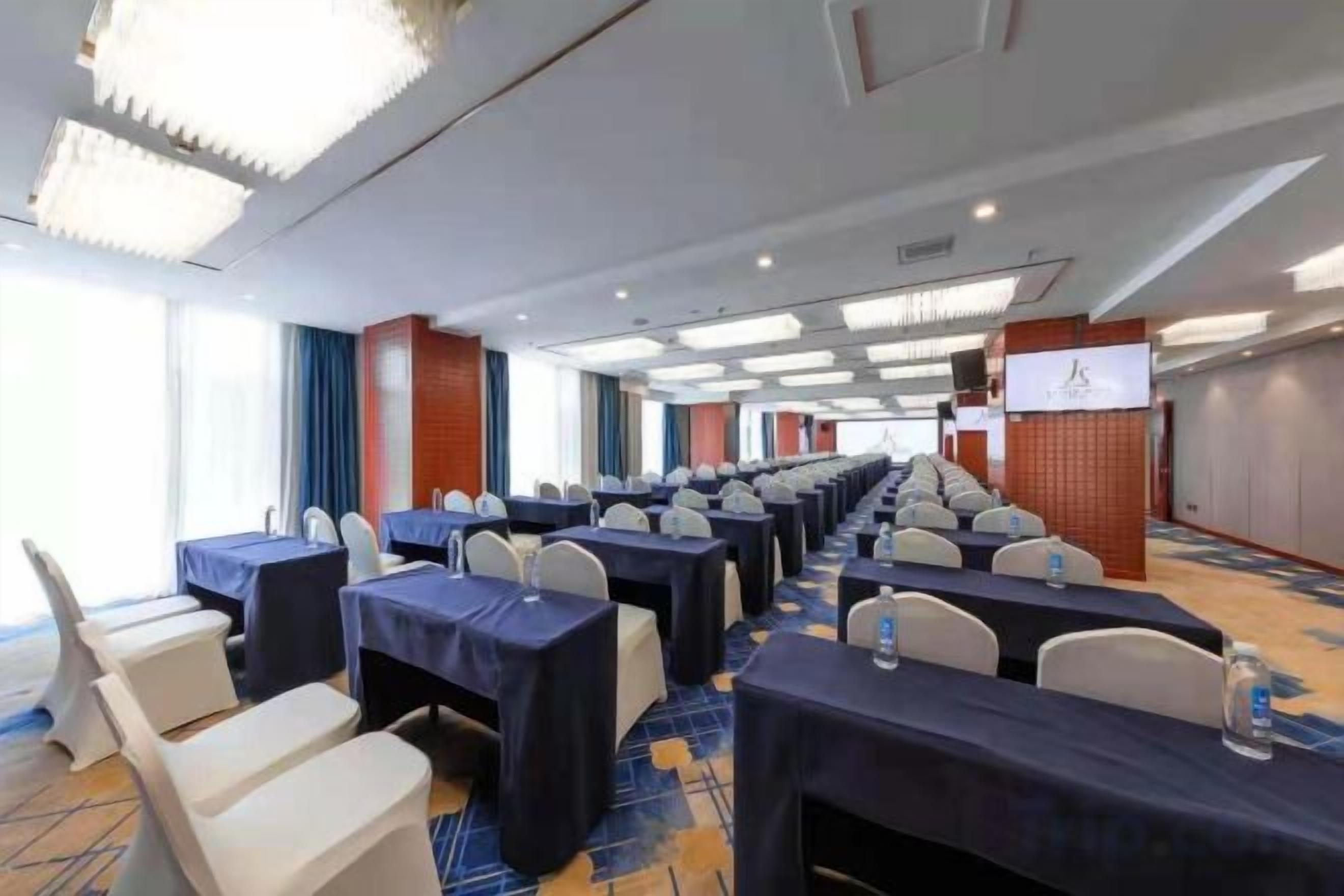 A conference room with rows of tables and chairs, a stage, and a large screen.